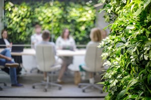 Ihmisiä istumassa viherseinien ja kasvillisuuden täyttämässä neuvotteluhuonessa sumeana taustalla